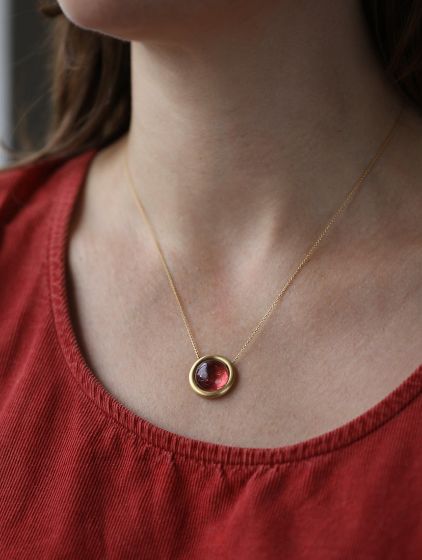 Round pink tourmaline pendant. 18ct yellow gold, satin finish. Worn on neck.