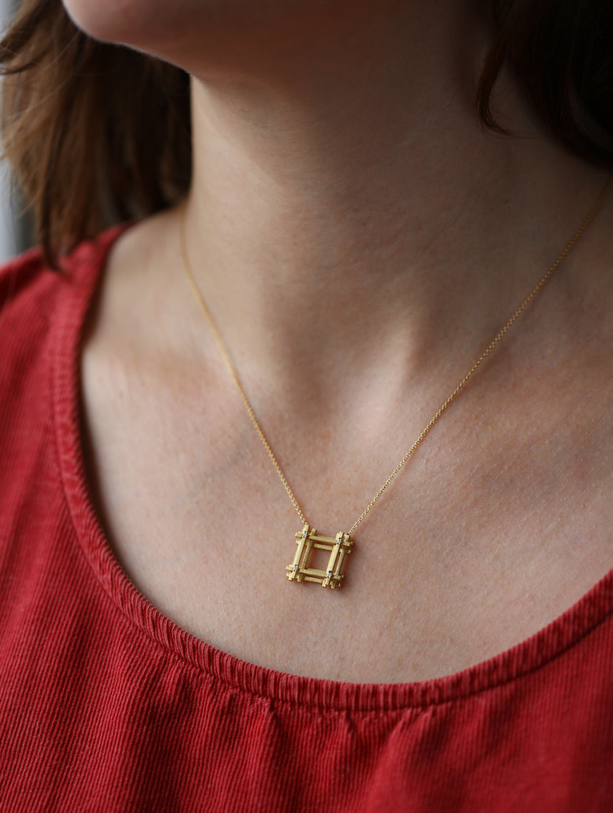 Geometric pendant with square structure detail and four tiny diamonds. 18ct yellow gold textured finish. On neck.