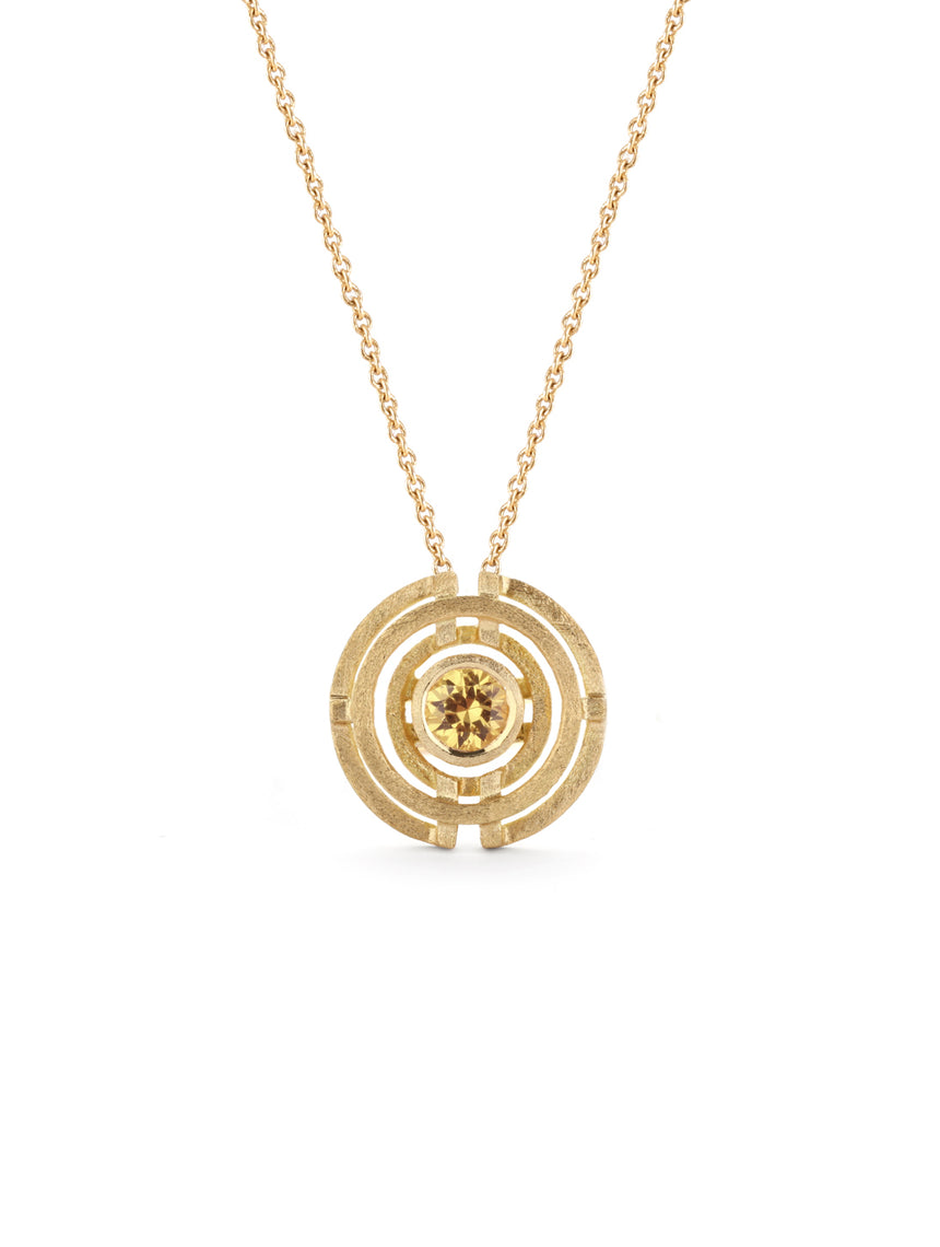 Geometric pendant with concentric circles surrounding yellow sapphire. 18ct yellow gold, textured finish.